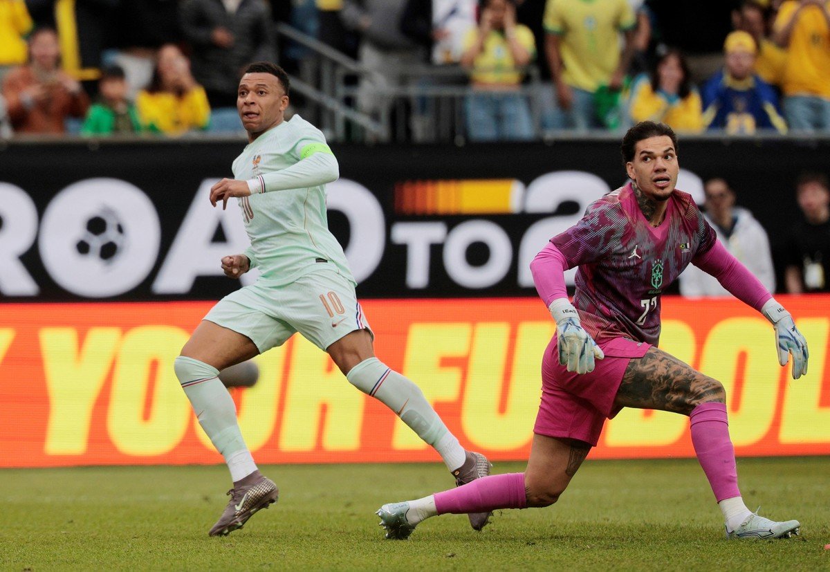 INICIO Kylian Mbappé con el uniforme de Francia y el portero Ederson de Brasil durante un partido de fútbol internacional, con un cartel de "ROAD TO 26" al fondo.