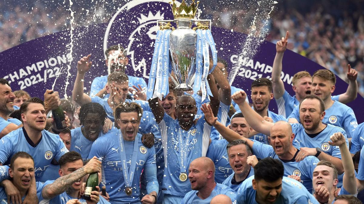 MANCHESTER CITY Jugadores del Manchester City celebrando el título de la Premier League 2021-22, levantando el trofeo entre confeti y champaña bajo el logo de Champions.