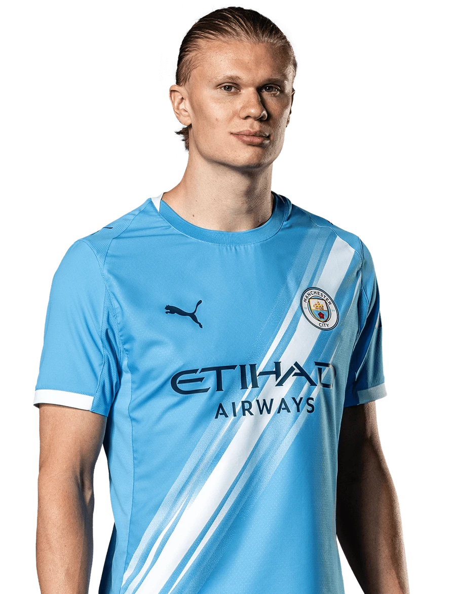 MANCHESTER CITY Retrato frontal de Erling Haaland posando con la camiseta de local del Manchester City sobre un fondo negro sólido.