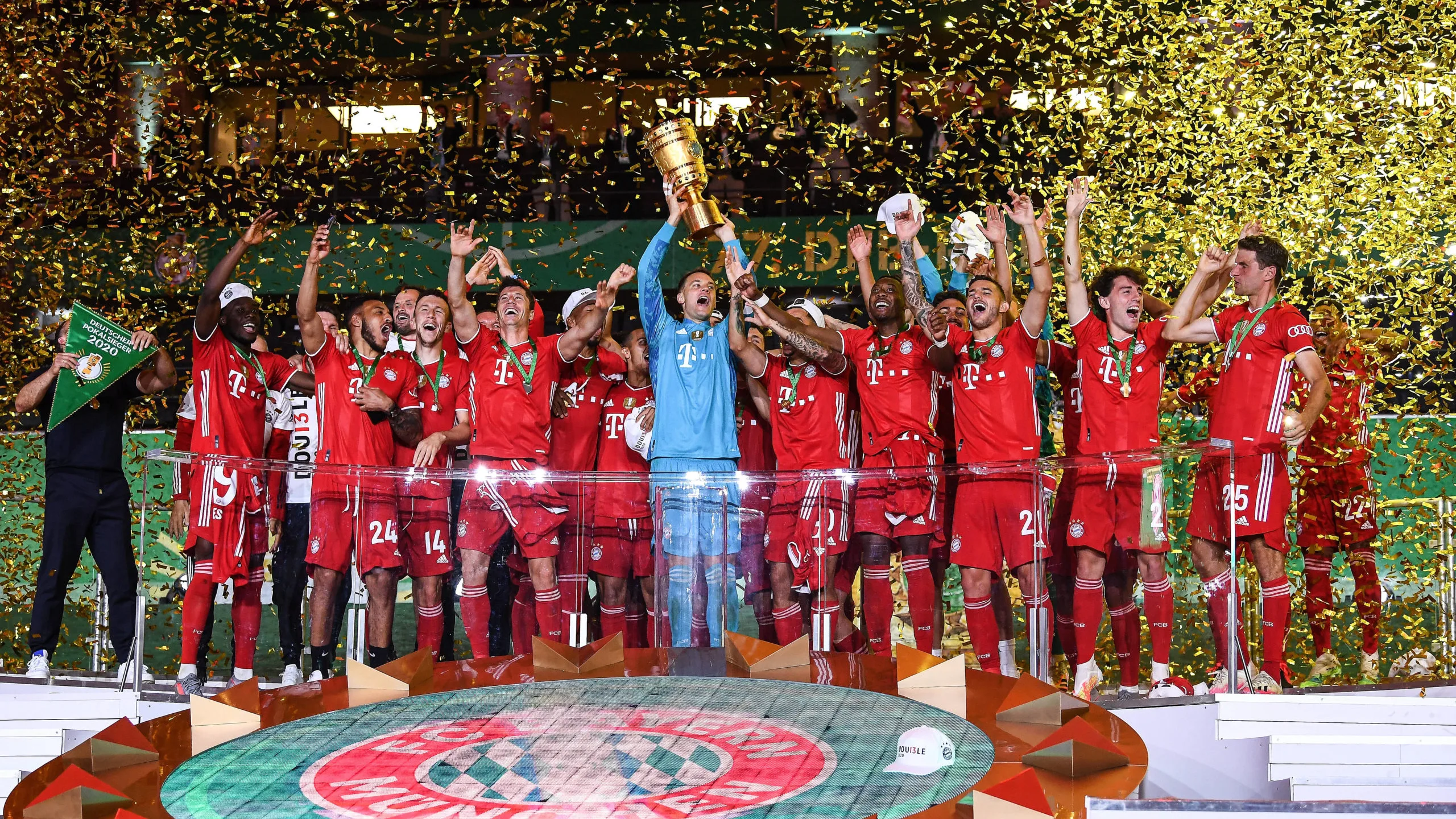 BAYERN MUNCHEN Manuel Neuer levantando el trofeo de la DFB-Pokal 2020 rodeado de jugadores del Bayern de Múnich bajo una lluvia de confeti dorado.