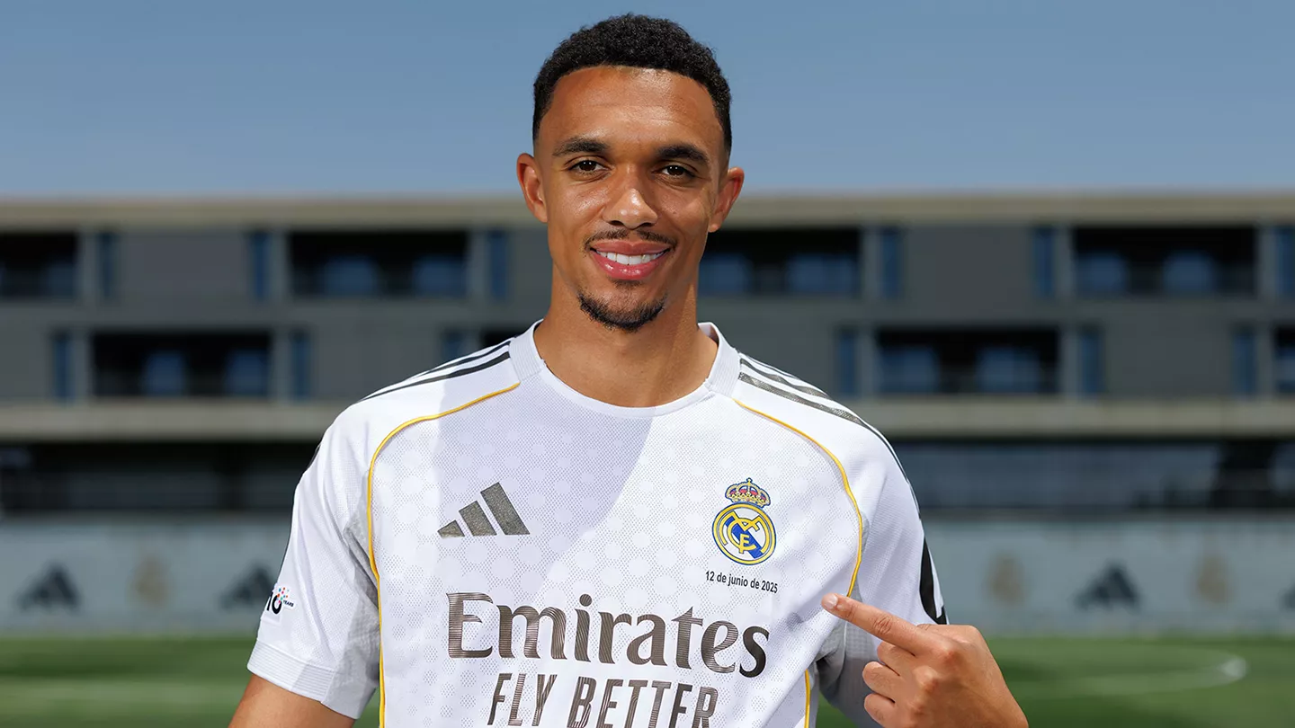 Fichajes confirmados Trent Alexander-Arnold posando con la camiseta oficial del Real Madrid y señalando el escudo en la Ciudad Deportiva de Valdebebas.