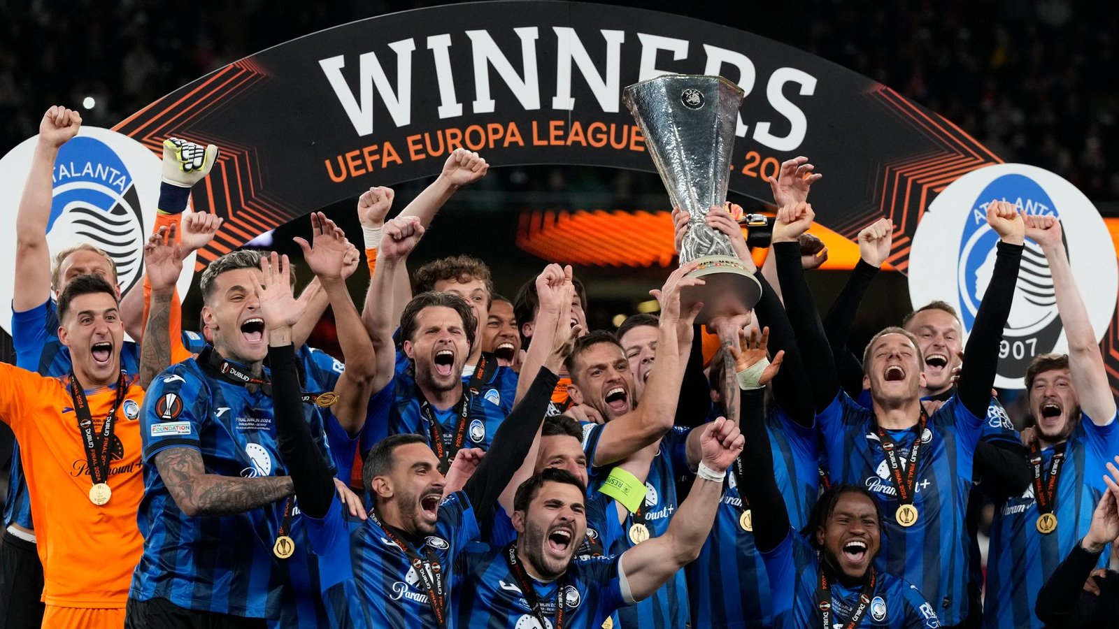 Leverkusen Jugadores de la Atalanta levantando el trofeo de la Europa League en un podio. Sobre ellos, un arco negro con la palabra "WINNERS" y el logo de la competición. Visten su clásica equipación nerazzurra y llevan medallas de oro al cuello.
